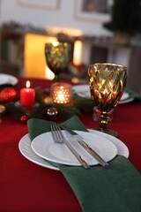 Stylish Christmas table setting with plates, glasses and burning candles in festive decorated room, closeup