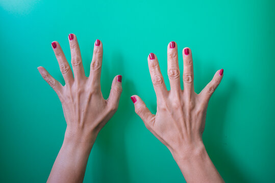Female hands with red nails on a green background. Top view. - Powered by Adobe