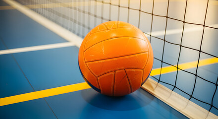 Orange volleyball rests near the net on a blue and yellow indoor sports court floor