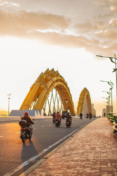 Dragon Bridge in Da Nang at sunset with orange sky and people riding motorbikes