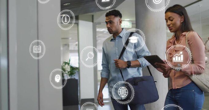 Two colleagues walking office corridor, woman tapping tablet causing HUD icons annotating tech data