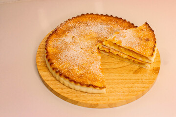 homemade round carved pie dusted with powdered sugar with a slice on top on wooden board