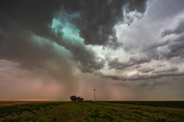 Storm clouds gathering over a small house on the horizon in a flat landscape.