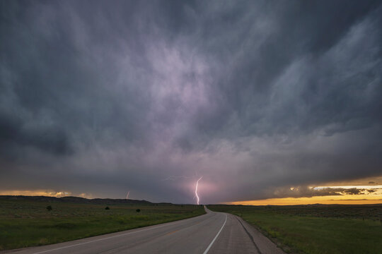 Sunset on WY Highway 59, view of the road ahead with cloud to ground lightning and black storm clouds. 