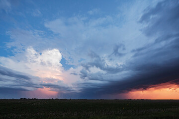 Approaching storm clouds with lightning in Nebraska, a blue sky background, glow on the horizon and a lightning bolt coming down to the ground. 