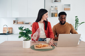 Interracial couple remote working during breakfast in kitchen