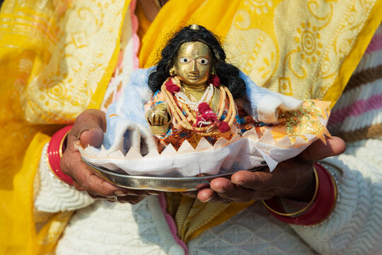 A woman holding a small puja offering, a shell shape with a small diety figure, a traditional religious offering to be made at a festival. 