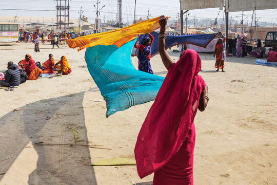 Maha Shivratri Hindu festival, a woman in a red sari and headscarf, waving blue and orange fabric above her head, drying the fabric after bathing in the river. 