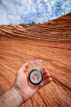 A hand holds a compass above wind-sculpted red sandstone in Zion National Park, capturing adventure, orientation, and natures textures under a sky of scattered clouds.