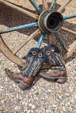 Worn Cowboy Boots Leaning on Vintage Wagon Wheel