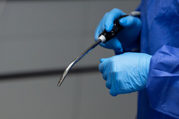 Medical theme, female hands wearing gloves and a surgical gown, holding a saliva ejector, dentistry.