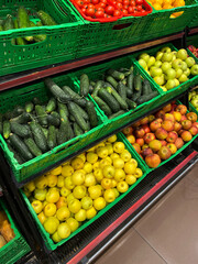 Fruits and vegetables on supermarket shelves. The photo shows cucumbers, apples, and tomatoes.