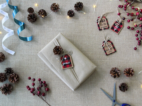 Flat lay overhead of Christmas gifts been wrapped with assorted holidays supplies on textured neutral surface using recycled kraft Paper. Holidays background with copy space. 