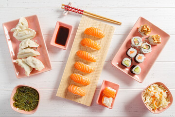 Assortiment de plats japonais : sushi, maki, California, gyozas, brochettes et salades sur table blanche avec sauces, baguettes et fleurs de cerisier