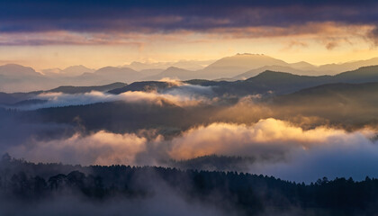 Misty mountain range at sunrise with golden light and dark clouds.