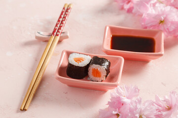 Maki saumon sur table colorée avec sauces soja, baguettes, vaisselle traditionnelle et fleurs de cerisier