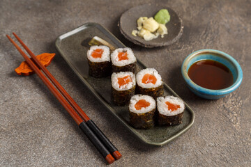 Maki saumon sur table foncée avec sauces soja, baguettes, vaisselle traditionnelle