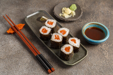 Maki saumon sur table foncée avec sauces soja, baguettes, vaisselle traditionnelle
