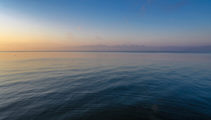 Calm ocean water under a twilight sky with distant mountains.