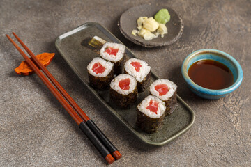 Maki saumon sur table foncée avec sauces soja, baguettes, vaisselle traditionnelle
