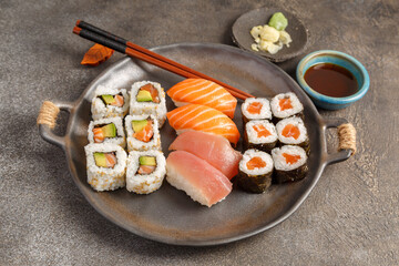 Assortiment de plats japonais : sushi, maki, California, gyozas, brochettes et salades sur table foncée avec sauces, baguettes. Vaisselle japonaise. 