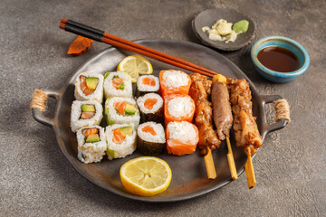 Assortiment de plats japonais : sushi, maki, California, gyozas, brochettes et salades sur table foncée avec sauces, baguettes. Vaisselle japonaise. 