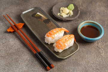 Sushi crevettes sur plat traditionnel avec gingembre, sauces et baguettes sur fond brun