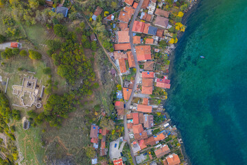 Aerial view of Lin village on Lake Ohrid, showing terracotta rooftops, turquoise water, and the ancient basilica ruins on the peninsula.