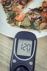 Glucose meter with result of sugar level and fresh baked vegetarian pizza. Nutrition during diabetes
