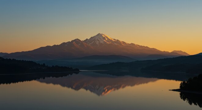 Majestic snow-capped mountain range reflects perfectly in calm body of water during sunrise