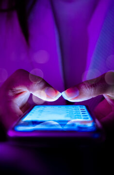 Close-up of hands typing on smartphone touchscreen at night, glowing blue screen, social media messaging, digital communication, technology lifestyle, modern mobile device, neon purple lighting