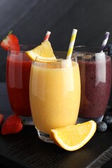 Different tasty smoothies in glasses and ingredients on black wooden table, closeup