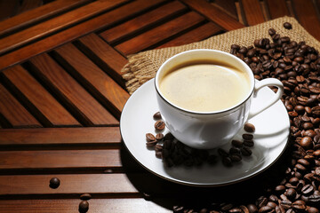 Aromatic coffee in cup and beans on wooden table, closeup. Space for text