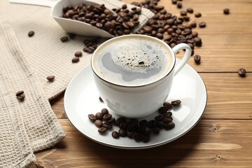 Aromatic coffee in cup and beans on wooden table, closeup