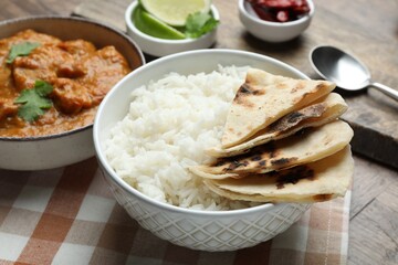 Delicious rice, lavash, chicken tikka masala and spices on wooden table, closeup
