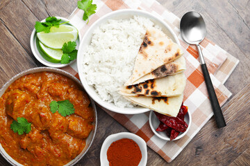 Delicious chicken tikka masala, rice, cilantro, lime, lavash and spices on wooden table, flat lay