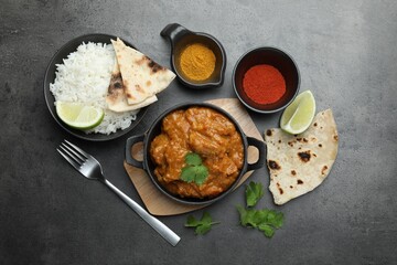 Delicious chicken tikka masala, rice, cilantro, lime, lavash and spices on grey textured table, flat lay