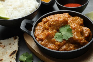 Delicious chicken tikka masala, cilantro, lavash, rice and paprika powder on grey table, closeup