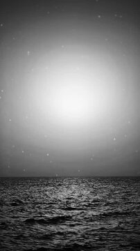 Vertical format wide shot animated loop showing a zoom effect in black and white of the sea and the sun with noise and flickr effect