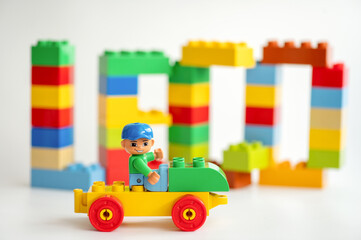 Naklejka premium A Lego construction worker minifigure sits on a toy car in front of Lego bricks on a white background