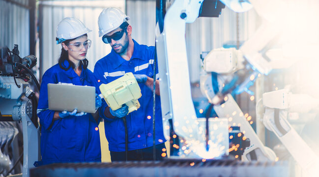Two engineers mechanic using computer controller Robotic arm for welding steel in steel factory workshop. Industry robot programming software for automated manufacturing technology - Powered by Adobe