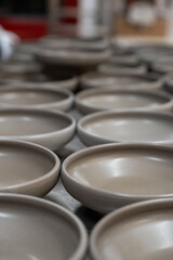 Numerous raw, unglazed ceramic plates are meticulously arranged in rows, likely drying on a table in a pottery workshop.