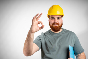 Young architect inspector man wearing builder safety helmet and using clipboard doing ok sign with fingers, excellent symbol