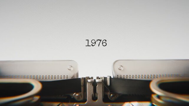 Old mechanical typewriter typing Year 1976 in a close-up view, with metal letters striking the white paper.
