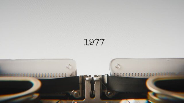 Old mechanical typewriter typing Year 1977 in a close-up view, with metal letters striking the white paper.