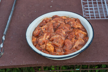 Bowl of marinated chicken pieces on rustic outdoor table, accompanied by metal skewer and grill rack. Ready for backyard grilling, casual outdoor cooking atmosphere