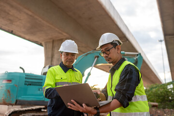 Civil engineers inspecting construction site under highway bridge using laptop