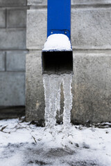 Blue metal downspout jammed with a frozen ice block. Vertical shot