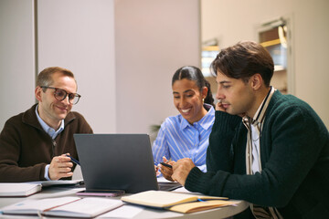 Multiethnic group of young adult and middle aged professionals collaborating at desk, Caucasian man, Black woman, Caucasian man discussing project using laptop and documents in office