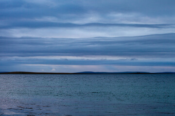 wide bands and ribbons of blue cloud sky over sea and island horizon in Orkney, Scotland, UK